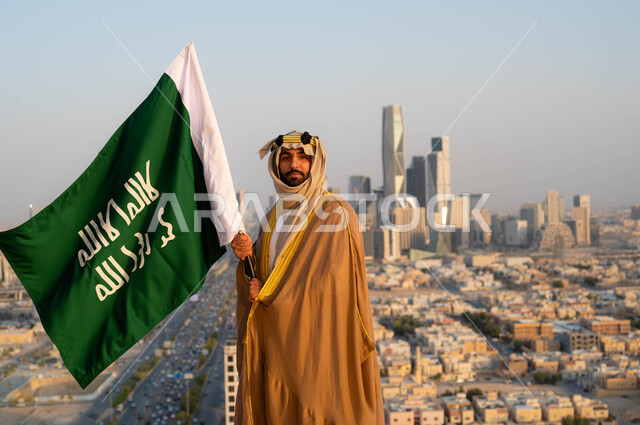 ذكرى يوم التأسيس في 22 شباط، توحيد البلاد في 1727 م، نظرات الفخر و الاعتزاز بالانتماء للوطن، الزي الشعبي التقليدي في المنطقة الوسطى ، مؤسس الدولة السعودية الاولى الامام محمد بن سعود, رجل عربي خليجي سعودي يرتدي البشت والغترة يحمل بيده علم التأسيس