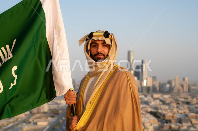 نظرات الفخر و الاعتزاز بالانتماء للوطن، الزي التقليدي في المنطقة الوسطى ، احياء ذكرى يوم التأسيس في 22 فبراير ، توحيد البلاد في 1727 م، مؤسس الدولة السعودية الاولى الامام محمد بن سعود, صورة مقربة لرجل عربي خليجي سعودي يرتدي البشت والغترة يحمل بيده علم التأسيس