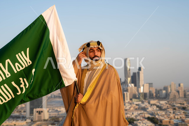 مؤسس الدولة السعودية الاولى الامام محمد بن سعود, الزي الشعبي التقليدي في المنطقة الوسطى ،الإحتفال بذكرى يوم التأسيس في 22 فبراير ،نظرات الفخر و الاعتزاز بالانتماء للوطن، تاريخ توحيد البلاد في 1727 م، رجل عربي خليجي سعودي يرتدي البشت والغترة يحمل بيده علم التأسيس