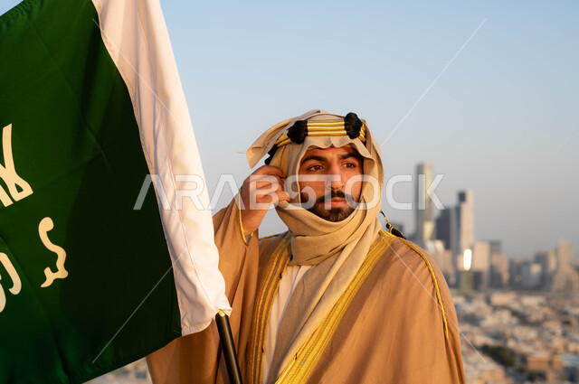 الزي التقليدي في المنطقة الوسطى ،الإحتفال بذكرى يوم التأسيس في 22 فبراير ،نظرات الفخر و الاعتزاز بالانتماء للوطن، توحيد البلاد في 1727 م، مؤسس الدولة السعودية الاولى الامام محمد بن سعود, صورة مقربة لرجل عربي خليجي سعودي يرتدي البشت والغترة يحمل بيده علم التأسيس