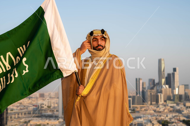 الزي الشعبي التقليدي في المنطقة الوسطى ،الإحتفال بذكرى يوم التأسيس في 22 فبراير ،نظرات الفخر و الاعتزاز بالانتماء للوطن، توحيد البلاد في 1727 م، مؤسس الدولة السعودية الاولى الامام محمد بن سعود, رجل عربي خليجي سعودي يرتدي البشت والغترة يحمل بيده علم التأسيس