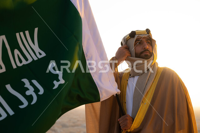 الإحتفال بذكرى يوم التأسيس في 22 فبراير ،نظرات الفخر و الاعتزاز بالانتماء للوطن، توحيد البلاد في 1727 م، مؤسس الدولة السعودية الاولى الامام محمد بن سعود, صورة مقربة لرجل عربي خليجي سعودي يرتدي البشت والغترة يحمل بيده علم التأسيس, الزي الشعبي في المنطقة الوسطى