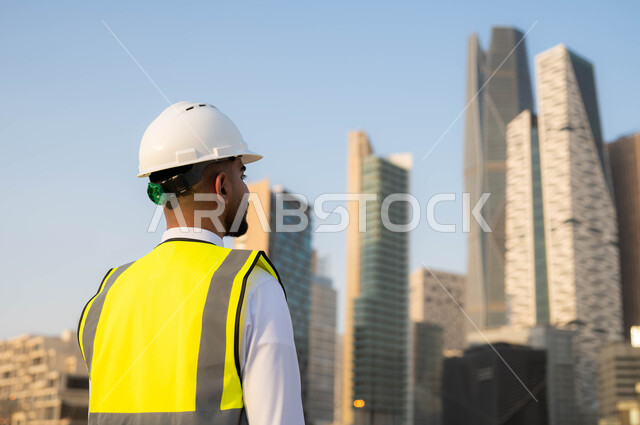 الاهتمام بالتطوير العمراني, الأبراج المالية والمنشآت الاقتصادية في مدينة الرياض, صورة من الخلف لمهندس معماري عربي خليجي سعودي يرتدي سترة الحماية والخوذة البيضاء ينظر لشيءما, مركز الملك عبدالله المالي(كافد) في المملكة, المعالم السياحية المشهورة في السعودية