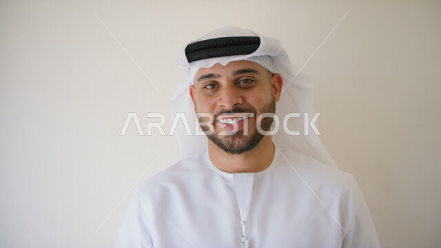 التقاط صورة شخصية للوثائق الرسمية, الإهتمام بالمظهر الخارجي، صورة مقربة لرجل عربي إماراتي خليجي مبتسم يرتدي الكندورة و الغترة الإماراتية وينظر إلى الكاميرا بإيماءات السعادة، خلفية بيضاء