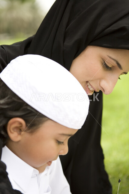 Weekend, playing with children, gestures indicating happiness, family trip on a sunny day, close-up of an Arab Emirati Gulf child playing with his mother in the park, the concept of a happy family, spending enjoyable family times