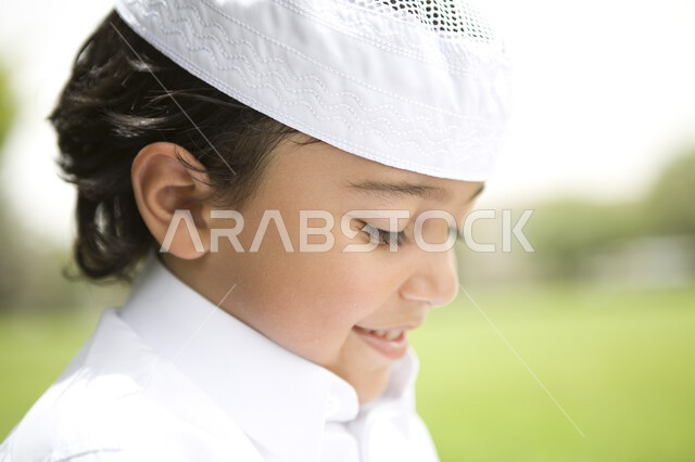 Gestures looking at something, having fun outside, close-up of a young boy wearing a white dress and a hat on his head in a public park, hiking outdoors, green nature background