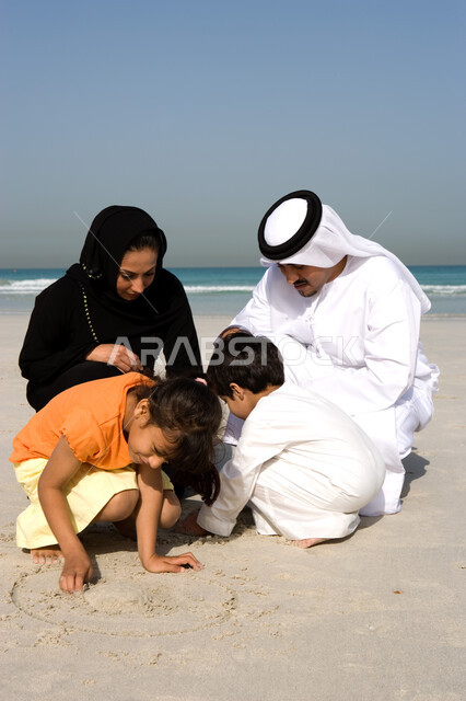 نشاطات ترفيهية للأطفال, قضاء أوقات صيفية ممتعة, الاستمتاع باللعب بالرمال على ساحل البحر مع العائلة,  أسرة عربية خليجية اماراتية تقوم بالرسم والكتابة على شاطئ البحر في إجازة الصيف، السياحة في دول الخليج العربي