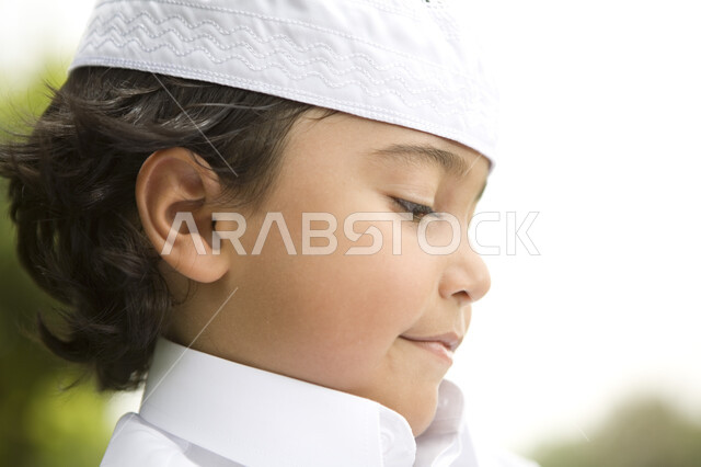 ايماءات النظر الى شيء ما, قضاء اوقات ممتعة في الخارج, صورة مقربة لصبي صغير يرتدي الثوب الابيض ويضع قبعة على رأسه في احدى الحدائق العامة, التنزه في الهواء الطلق, خلفية الطبيعة الخضراء