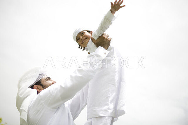 Enjoying playing on a sunny day, spending quality time with children, an Emirati Arab Gulf father playing with his son and raising him high, spending quality time in the garden, a happy family trip, spending an enjoyable summer vacation, enjoying playing 