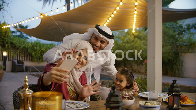 إجراء مكالمة فيديو عبر الجوال, صورة مقربه لعائلة عربية إماراتية خليجية تجلس على مائدة الإفطار في شهر رمضان المبارك ،تناول وجبة الفطور في إحدى المطاعم, زينة و أضواء الشهر الفضيل, توثيق اللحظات السعيدة العائلية بالتقاط صور السيلفي التذكارية