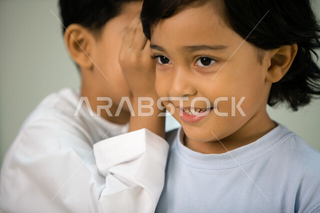 الهمس والهدوء أثناء الكلام, إخبار الأسرار للأصدقاء, مشاركة الأخبار السرية لزملاء المدرسة, صورة مقربة لولد عربي خليجي إماراتي يقوم بمشاركة سر ما لصديقه, التحدث بصوت منخفض والمحافظة على كتمان السر