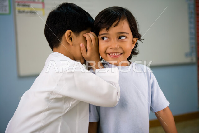 إخبار الأسرار للأصدقاء, مشاركة الأخبار السرية لزملاء المدرسة, صورة مقربة لولد عربي خليجي إماراتي يقوم بمشاركة سر ما لصديقه, التحدث بصوت منخفض والمحافظة على كتمان السر, الهمس والهدوء أثناء الكلام