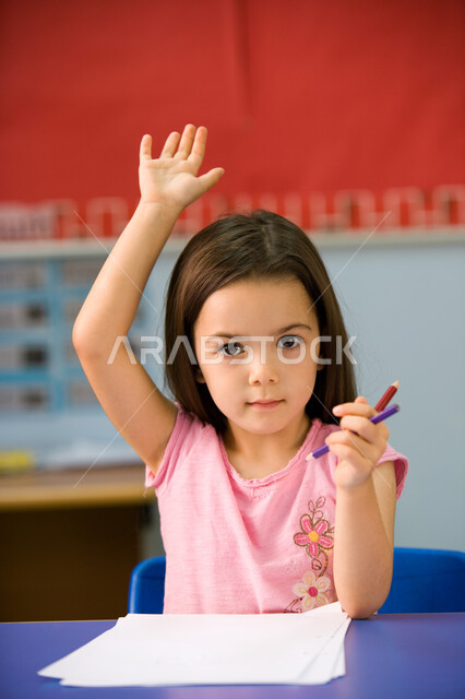 المشاركة مع المعلمة برفع اليد, الالتزام والانضباط بقواعد الفصل الدراسي, صورة مقربة لطالبة مرحلة تمهيدي عربية خليجية إماراتية ترتدي الزي الكاجوال ترفع يدها عاليا, المدارس التعليمية في الإمارات العربية المتحدة, الاهتمام والعناية بأطفال الروضة
