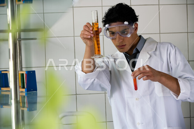 Studies and experiments in a sophisticated practical environment, research and development and conducting chemical reactions, an Arab Gulf Emirati university student conducting a scientific experiment in the laboratory, wearing protective glasses and a wh