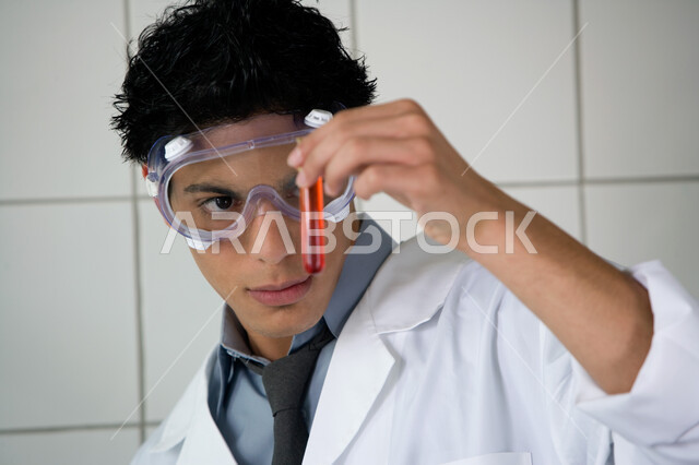 ارتداء نظارة الوقاية والمعطف الأبيض, الدراسات والتجارب في بيئة عملية متطورة, البحث والتطوير وإجراء التفاعلات الكيميائية, صورة مقربة لطالب جامعي عربي خليجي إماراتي يقوم بتجربة علمية في المختبر, اكتساب المعرفة والخبرة بإيماءات الدقة والتركيز في التجربة