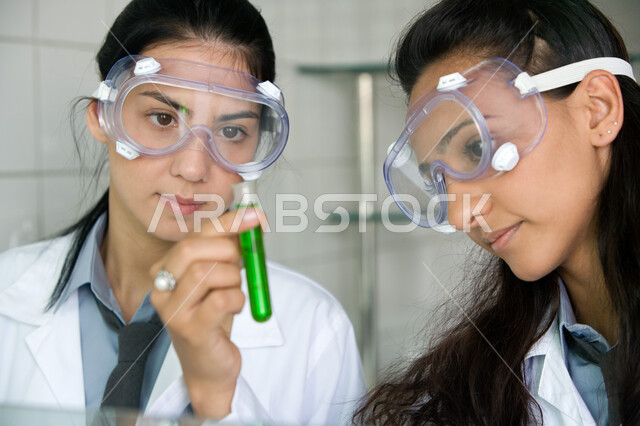اكتساب المعرفة من خلال التجارب العلمية الحديثة, صورة مقربة لطالبتين عربيتين خليجيتين إماراتيتين تقومان بتجربة كيميائية في مختبر المدرسة, ارتداء النظارات الوقائية والمعطف الطبي الأبيض, الأنشطة التعليمية والاستفادة العملية من التجارب