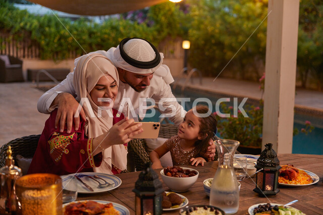 المأكولات الشهية والأصناف المتنوعة على سفرة الافطار، الإستمتاع بالأجواء الرمضانيه مع الأهل، التقاط صورة عائليه تذكاريه، عائله عربيه خليجيه اماراتية تجلس على مائدة الطعام وتقوم بأخذ الصور عبر الهاتف المحمول، مفهوم المحبة والترابط الأسري.