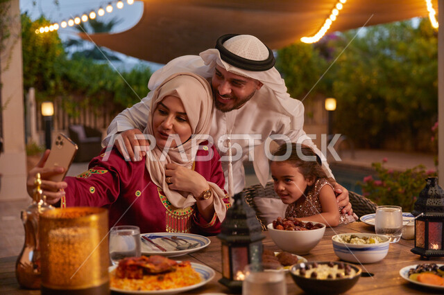 الأصناف المتنوعة والمأكولات الشهية على سفرة الافطار، الإستمتاع بالأجواء الرمضانيه مع الأهل، التقاط صورة عائليه تذكاريه، عائله عربيه خليجيه اماراتية تجلس على مائدة الطعام وتقوم بأخذ الصور عبر الهاتف المحمول، مفهوم المحبة والترابط الأسري.