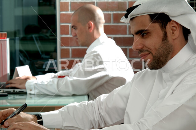 المساهمة في تطوير المهارات والخبرات, التمتع بصفة الرياده والاصرار على النجاح, ارتداء الزي الإماراتي التقليدي، مهن ووظائف إماراتية، شركات ومكاتب خليجية في الإمارات العربية المتحدة، صورة مقربة لزميلا عمل عربيان إماراتيان خليجيان يجلسان في مقر الشركة
