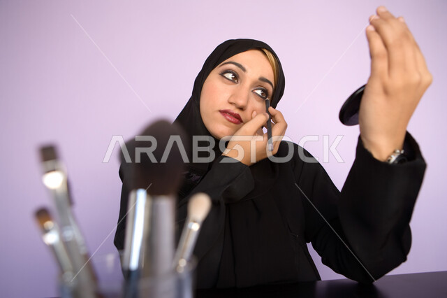 Beautification and adornment with cosmetic tools, marketing of makeup products and cosmetics in stores and online, the concept of caring for beauty and skin, a portrait of an Arab Gulf Emirati beautician holding a kohl pencil to highlight the eye and look