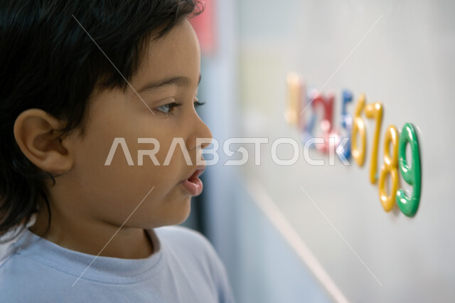 أهمية تعلم الأرقام والأعداد الانجليزية, صورة مقربة من الجانب لطالب تمهيدي عربي خليجي إماراتي يرتدي الزي الكاجوال يقف أمام السبورة, حصص اللغة الإنجليزية في مدارس الإمارات العربية المتحدة, تطور طرق التعليم وتنمية الذكاء لدى الأولاد 