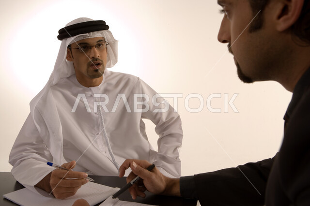 مناقشة وتنظيم العمل, الشراكة والتعاون في انجاز العمل, توسيع نطاق الاعمال, إعداد خطط الاعمال الاستراتيجية, مهن ووظائف اماراتية, رجل عربي خليجي اماراتي يرتدي الكندورة الاماراتية ورجل بالبدلة الرسمية في غرفة الإجتماعات داخل مقر الشركة