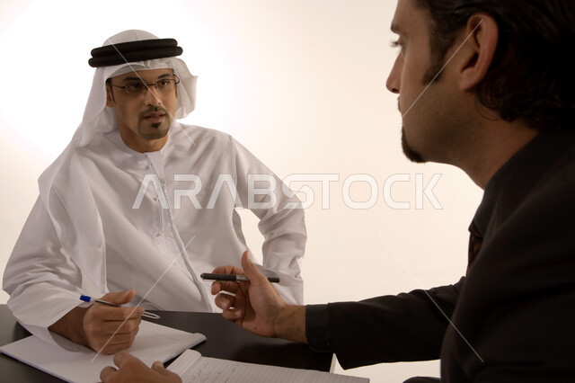 مناقشة وتنظيم العمل, الشراكة والتعاون في انجاز العمل, توسيع نطاق الاعمال, إعداد خطط الاعمال الاستراتيجية, مهن ووظائف اماراتية, رجل عربي خليجي اماراتي يرتدي الكندورة الاماراتية ورجل بالبدلة الرسمية في غرفة الإجتماعات داخل مقر الشركة
