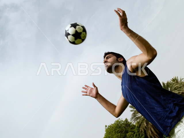 Recreational activities and youth sports, a close-up of an Arab Emirati man playing football, enthusiasm and passion to shoot goals, jump high to kick and shoot the ball, basic skills in playing football, practicing his favorite hobby in the garden.