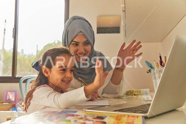 عرض بث مباشر على إحدى وسائل السوشل ميديا، إجراء مكالمة فيديو عبر الحاسب المحمول، أم عربية خليجية اماراتية محجبة تقوم بالترحيب والتواصل اونلاين مع الاقارب والاصدقاء  برفقة ابنتها، متابعة منصات التعليم الالكتروني المتاحة عبر الانترنت.  