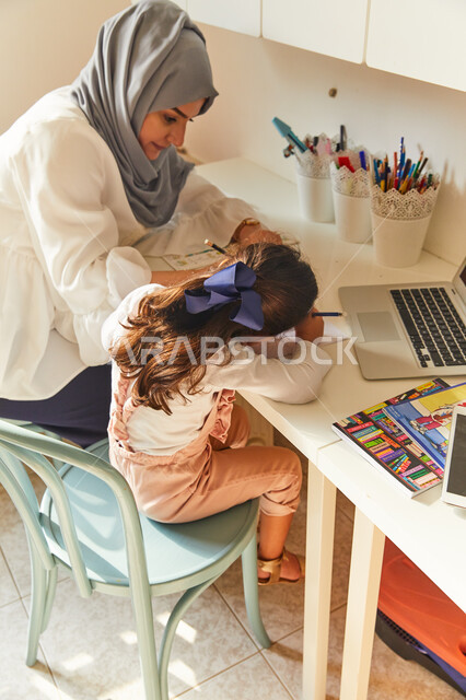 معلمة خصوصي لمتابعة الدروس في المنزل، حل الواجبات المنزليه، ادخال التقنية والتكنولوجيا في مجال التعليم، متابعة منصات التعليم الالكتروني المتاحة عبر الانترنت بإستخدام الحاسب المحمول، أم عربية خليجة اماراتية محجبة تقوم بتعليم وتدريس ابنتها