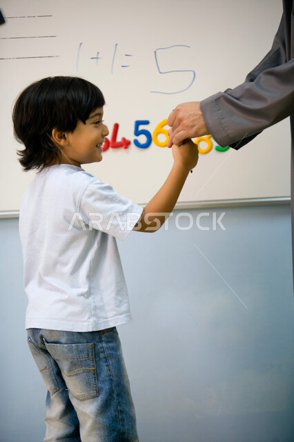 تنمية المهارات الذهنية لدى الأطفال, معلمة عربية خليجية إماراتية تقوم بمساعدة الطلاب داخل الفصل بإيماءات السعادة والسرور, القيام بالعمليات الحسابية على السبورة, الأساليب الحديثة في التعليم الاستنتاجي, المشاركة العملية ومحاكاة ذكاء الطالب