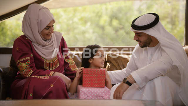 التسامر والضحك مع الأبناء, أجواء عائلية سعيدة مليئة بالحب, الاحتفال بقدوم العيد المبارك، عائلة عربية خليجية اماراتية يجلسون في غرفة المعيشة بإيماءات السعادة والفرح، ارتداء الزي الإماراتي وتقديم الهدايا في الأعياد والمناسبات الإسلامية