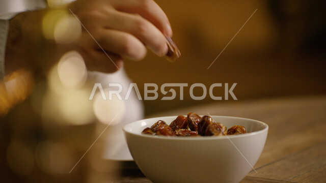 A meal with high nutritional value, a close-up of the hand of an Arab Emirati Gulf man eating some dates, a spiritual Ramadan atmosphere, national local products, lights and decorations for the holy month of Ramadan