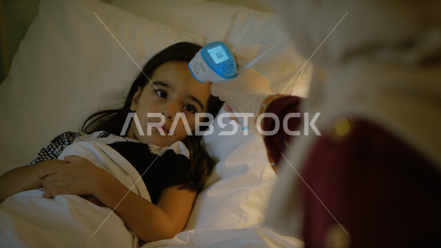 الاهتمام والاعتناء بالأبناء و رعايتهم, شعور الشخص المصاب بالإرهاق وأهمية العناية به، صورة مقربة لأم عربيه خليجية اماراتية محجبة ترتدي العباءة المطرزة تقوم بفحص درجة حرارة ابنتها بواسطة جهاز كاشف الكورونا، أخذ الحيطة و الحذر والوقاية لتجنب العدوى بالفايروس