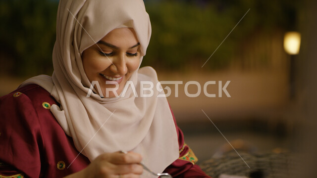 الاستمتاع في أوقات الفراغ في إحدى المطاعم, صورة مقربه لإمرأة عربيه إماراتيه خليجيه محجبه مبتسمة تنظر إلى شيء ما, تناول وجبه الإفطار مع العائلة في الخارج, ايماءات تدل على السعادة, قضاء أوقات ممتعه في العطلة الصيفيه, التنزه في الهواء الطلق