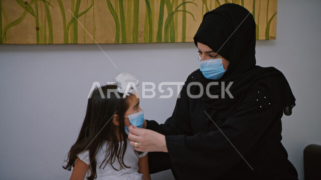  قضاء أوقات ممتعه في العطلة الصيفيه والاستمتاع بالخروج مع العائله، الاحتراز والوقاية من فايروس كورونا, إتباع إجراءات وزارة الصحة الوقائيه، سيدة عربية خليجية إماراتية تقوم بوضع كمامة الوقائية من كوفيد-١٩ لابنتها ويستعدون للذهاب من المنزل .