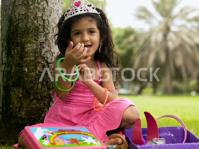 الاهتمام بالأنوثة والأناقة منذ الصغر, تعزيز الثقة بالنفس وتقوية الشخصية للأطفال, تقمص وتقليد شخصيات الأميرات الكرتونية, فتاة صغيرة عربية خليجية إماراتية ترتدي فستان وتاج الأميرة تلعب في مجوهرات البنات في إحدى الحدائق العامة، ألعاب وأنشطة ترفيهية ممتعة.