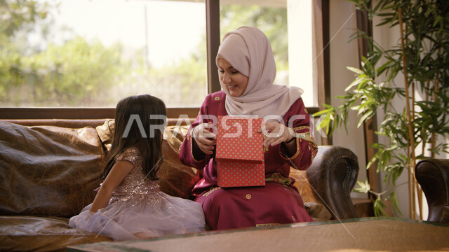 الاحتفال بالمناسبات والأعياد  بإيماءات السعادة والدهشة والفرح, صورة مقربه لفتاة عربيه خليجية اماراتيه  تقوم بتقديم الهدايا لوالدتها بمناسبة عيد الأم, أجواء عائلية حماسية مليئة بالحب, الاحتفال بقدوم العيد المبارك, أجواء عائليه مليئة بالحب