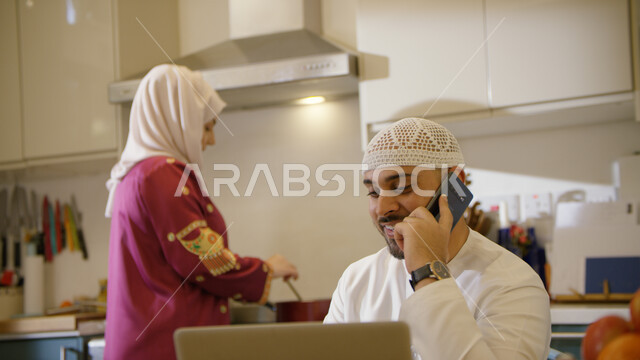 إجراء مكالمة صوتية عبر الجوال, قضاء أوقات ممتعه في المطبخ مع الزوجة، رجل عربي خليجي اماراتي يرتدي الكندوره والطاقية يقوم بالعمل أونلاين عبر الحاسوب، امرأه عربيه خليجيه اماراتيه محجبه ترتدي عباءه مطرزه تقوم بتحضير الطعام، متابعة آخر أخبار السوشال ميديا .