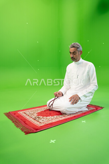 التسبيح وذكر الله تعالى، كروما لرجل عربي خليجي سعودي يرتدي  الثوب التقليدي يحمل بيده السبحة ويجلس على سجادة الصلاة، العبادة والتقرب إلى الله، أدعية وأذكار إسلامية، إسلاميات وعبادة، خلفية خضراء