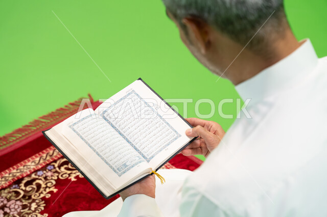 تلاوة وحفظ القرآن الكريم، التسبيح وذكر الله تعالى، كروما مقربة لرجل عربي خليجي سعودي يرتدي الثوب التقليدي يحمل بيده المصحف الشريف ويجلس على سجادة الصلاة، العبادة والتقرب إلى الله، أدعية وأذكار إسلامية، إسلاميات وعبادة، خلفية خضراء