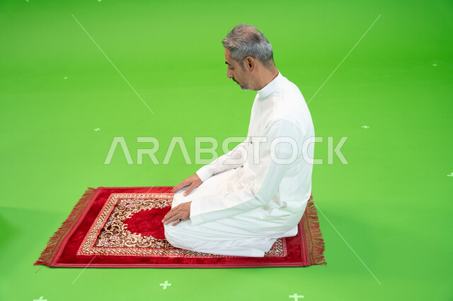 Worship and closeness to God, the concept of the pillars of Islam, the performance of religious duties, the chroma of a Saudi Arabian Gulf man wearing traditional dress standing on a prayer rug, green background