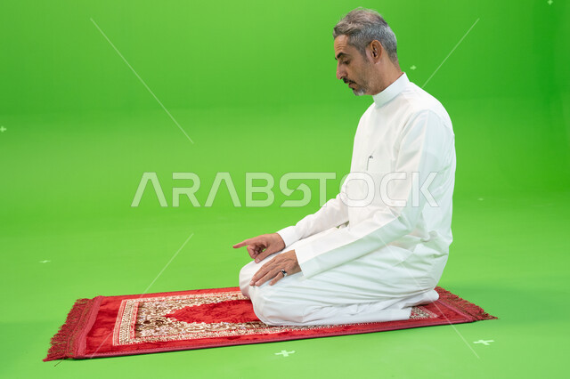 الخشوع في الصلاة والتضرع الى الله ، الجلوس للتشهد على سجادة الصلاة, كروما لرجل عربي خليجي سعودي يرتدي الزي التقليدي يجلس على سجادة الصلاة ،العبادة والتقرب إلى الله، مفهوم أركان الإسلام، اسلاميات وعبادة، خلفية خضراء