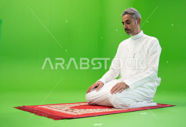 أداء الفرائض الدينية، مفهوم أركان الإسلام، كروما لرجل عربي خليجي سعودي يرتدي الزي التقليدي يجلس على سجادة الصلاة ،العبادة والتقرب إلى الله، خلفية خضراء