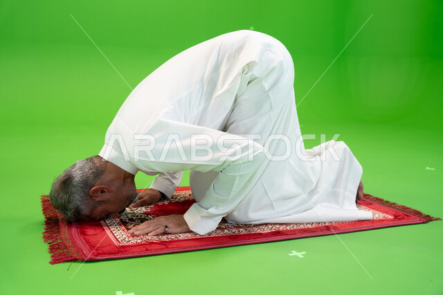 إصلاح النفس بالتذلل لرب العالمين، التضرع والخشوع أثناء السجود، أداء الفرائض الدينية، مفهوم أركان الإسلام، كروما لرجل عربي خليجي سعودي يرتدي الزي التقليدي يجلس على سجادة الصلاة ،العبادة والتقرب إلى الله، صورة الجسم بالطول الكامل ،خلفية خضراء