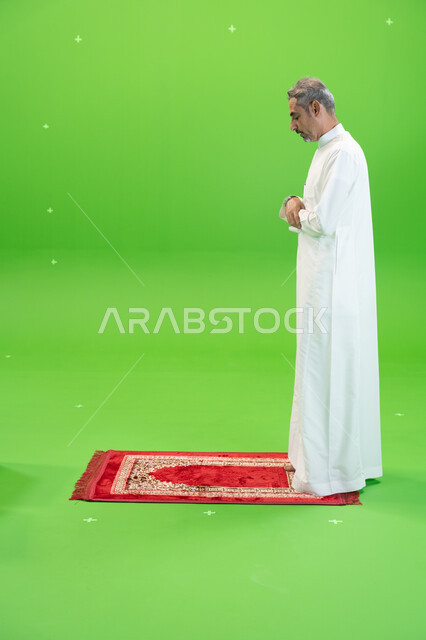 مفهوم أركان الإسلام ،أداء فرائض الصلاة بأوقاتها، كروما لرجل عربي خليجي سعودي يرتدي الزي التقليدي يقف على سجادة الصلاة ،العبادة والتقرب إلى الله، إسلاميات وعبادة، صورة الجسم بالطول الكامل ،خلفية خضراء