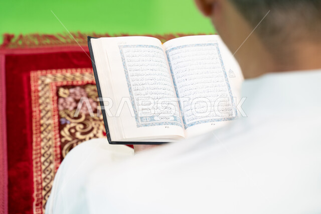  إسلاميات وعبادة، تلاوة وحفظ القرآن الكريم، التسبيح وذكر الله تعالى، كروما مقربة من الخلف لرجل عربي خليجي سعودي يرتدي الثوب التقليدي يحمل بيده المصحف الشريف ويجلس على سجادة الصلاة، العبادة والتقرب إلى الله، أدعية وأذكار إسلامية، خلفية خضراء