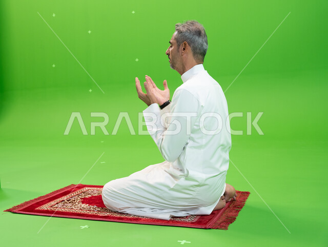 التقرب الى الله بالأعمال الصالحة، التذلل و الطلب من الله تعالى, كروما مقربة لرجل عربي خليجي سعودي يرتدي الزي التقليدي يرفع يديه ويدعي بإيماءات التوسل و الخشوع، اسلاميات وعبادة، خلفية خضراء