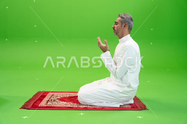 التقرب الى الله بالأعمال الصالحة، التذلل و الطلب من الله تعالى, كروما مقربة لرجل عربي خليجي سعودي يرتدي الزي التقليدي يرفع يديه ويدعي بإيماءات التوسل و الخشوع، اسلاميات وعبادة، خلفية خضراء