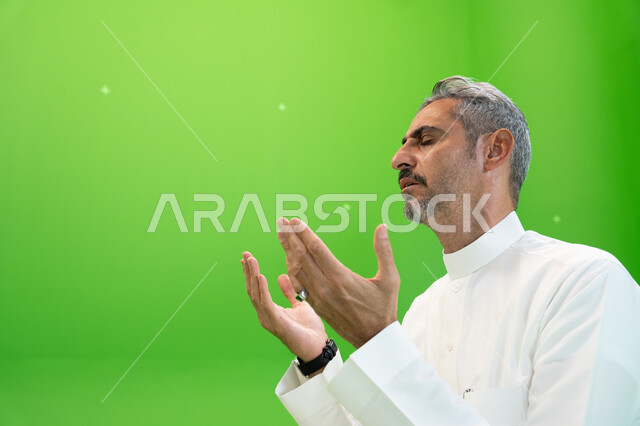 التقرب الى الله بالأعمال الصالحة، التذلل و الطلب من الله تعالى, كروما مقربة لرجل عربي خليجي سعودي يرتدي الزي التقليدي يرفع يديه ويدعي بإيماءات التوسل و الخشوع، اسلاميات وعبادة، خلفية خضراء
